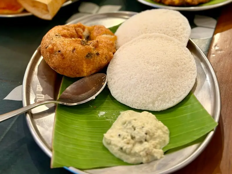 Idli, vada and dosa with coconut chutney on a steel plate lined with banana leaf