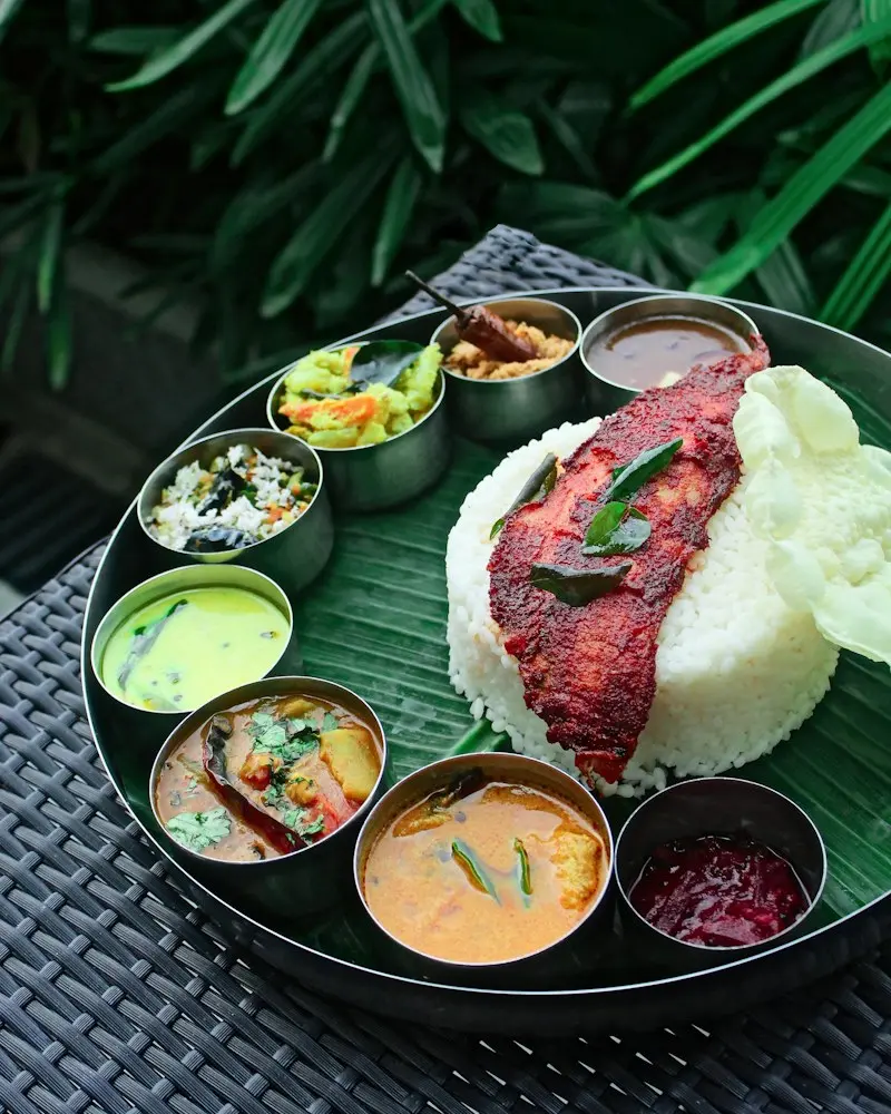 Fish fry on rice with small bowls of curries around it on a banana leaf