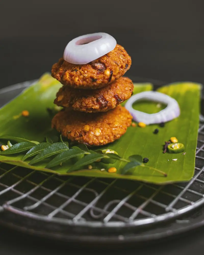 Stack of three lentil vadas with onion rings on a banana leaf